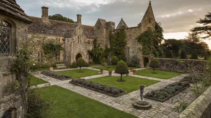 The Forecourt garden, with stone-paved paths, square lawns and small trees, with the house behind, at Nymans, West Sussex